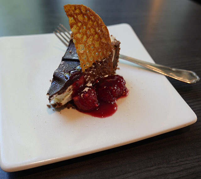 A piece of chocolate dessert sat on a white square plate with a fork resting to one side