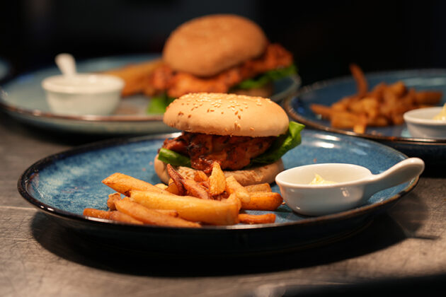 A plate with chips, a burger in a bun and some white sauce in a small white container