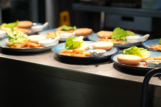 Serveral plates containing chips, a burger in a bun and some white sauce in a small white container