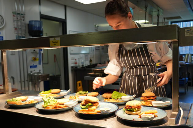 Serveral plates containing chips, a burger in a bun and some white sauce in a small white container