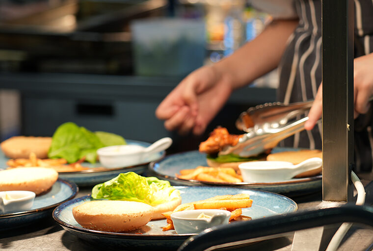 Serveral plates containing chips, a burger in a bun and some white sauce in a small white container
